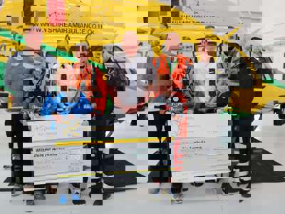 A group of visitors in front of the helicopter holding a large cheque inside the hanger A group of visitors in front of the helicopter holding a large cheque inside the hanger