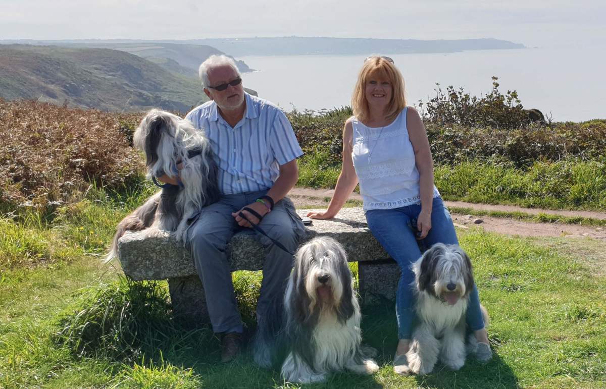 A couple sat on a bench overlooking a coastal path with their three dogs. A couple sat on a bench overlooking a coastal path with their three dogs.