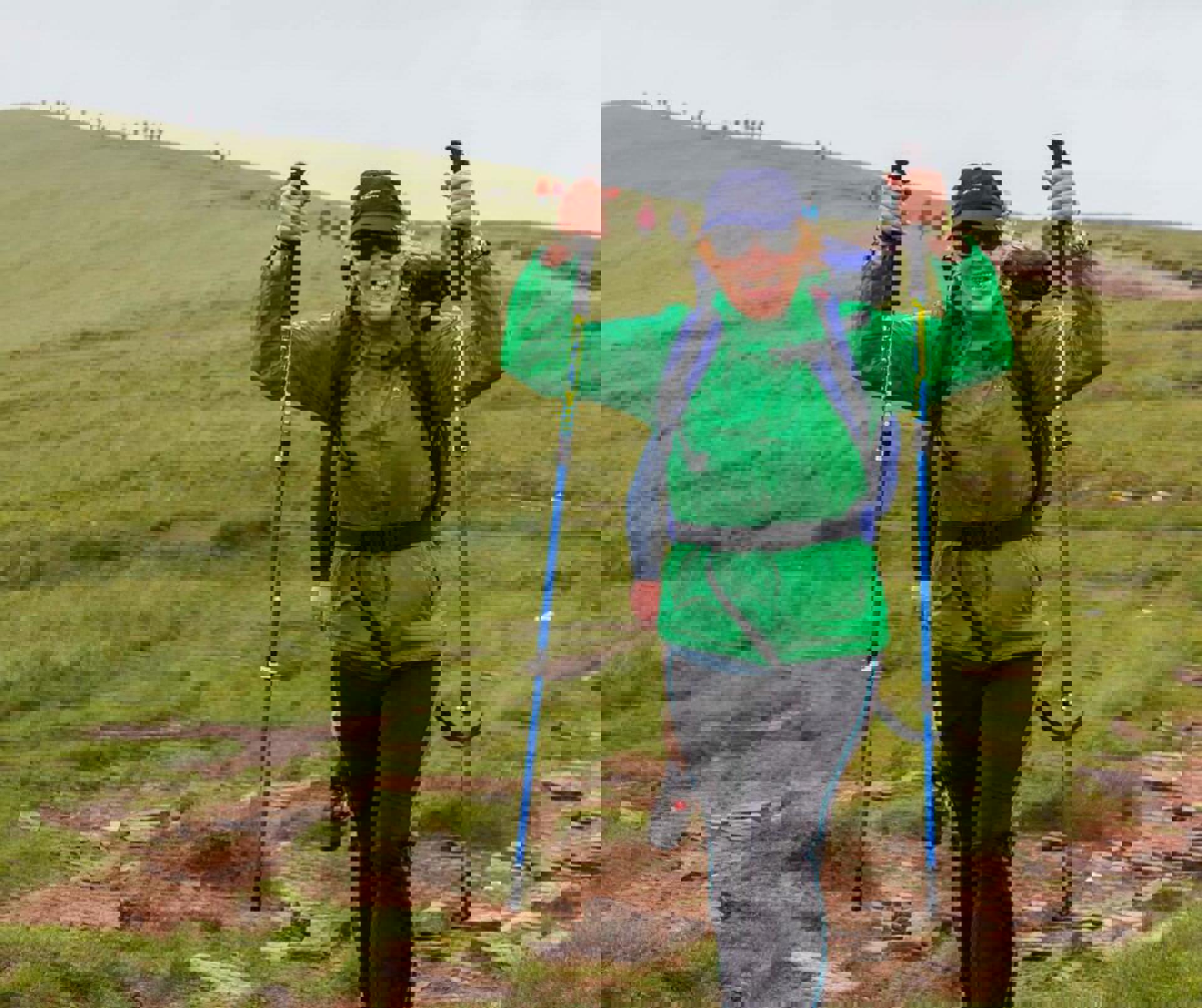 A person wearing a green raincoat and blue backpack, holding walking poles in the air A person wearing a green raincoat and blue backpack, holding walking poles in the air