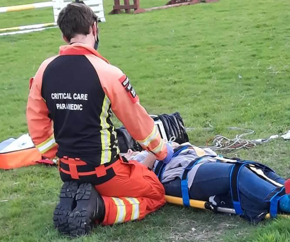 A patient laying on a stretcher with a critical care paramedic knelt by their side A patient laying on a stretcher with a critical care paramedic knelt by their side