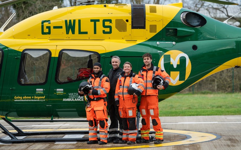 A group of air ambulance colleagues standing in front of a yellow and green helicopter