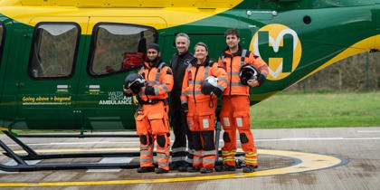 A group of air ambulance colleagues standing in front of a yellow and green helicopter A group of air ambulance colleagues standing in front of a yellow and green helicopter