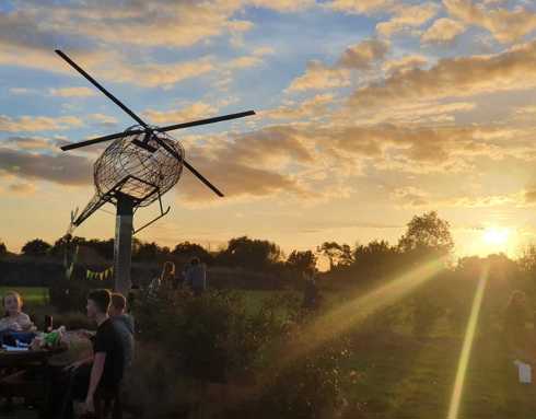 People enjoying the sunset, below a model of the helicopter, at the Wiltshire Air Ambulance airbase