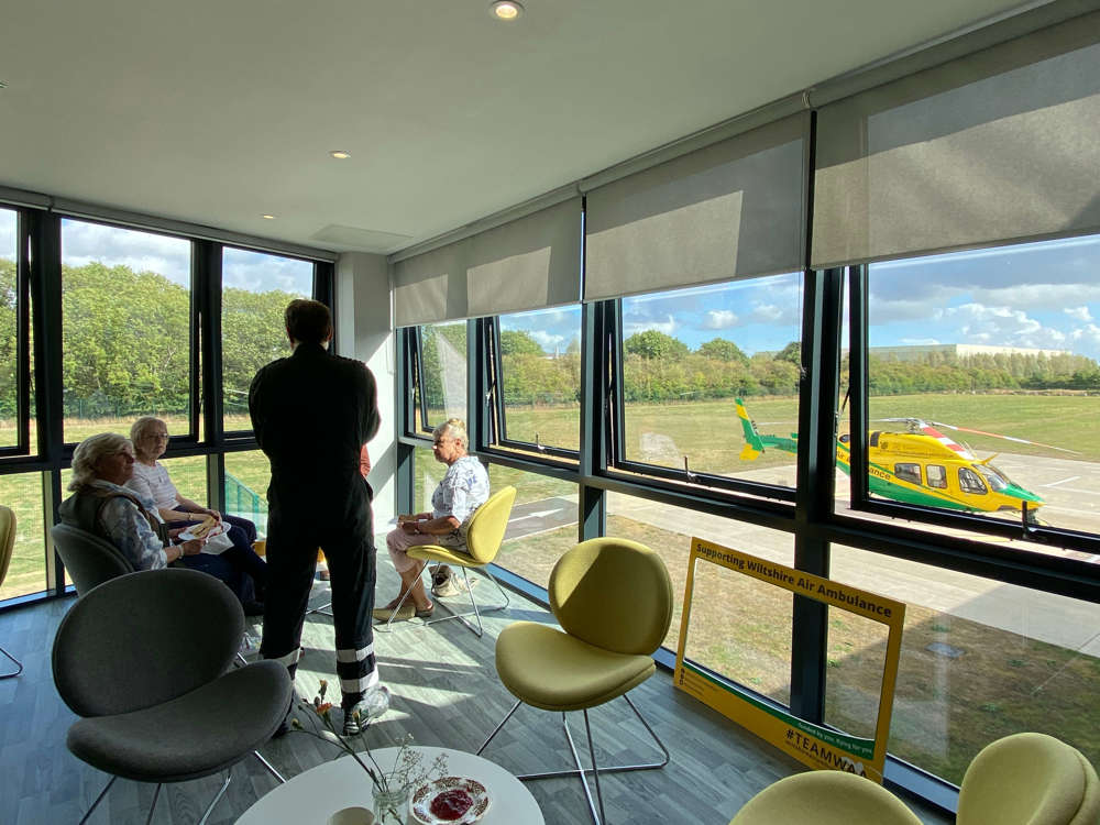 Pilot talking to 3 supporters in a room overlooking the Wiltshire Air Ambulance helicopter and helipad Pilot talking to 3 supporters in a room overlooking the Wiltshire Air Ambulance helicopter and helipad