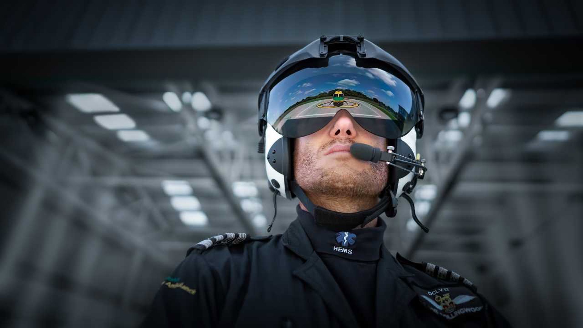 Pilot Rob Collingwood looking at the helicopter whilst wearing a flight helmet and visor. There is a reflection of the helicopter in the visor.