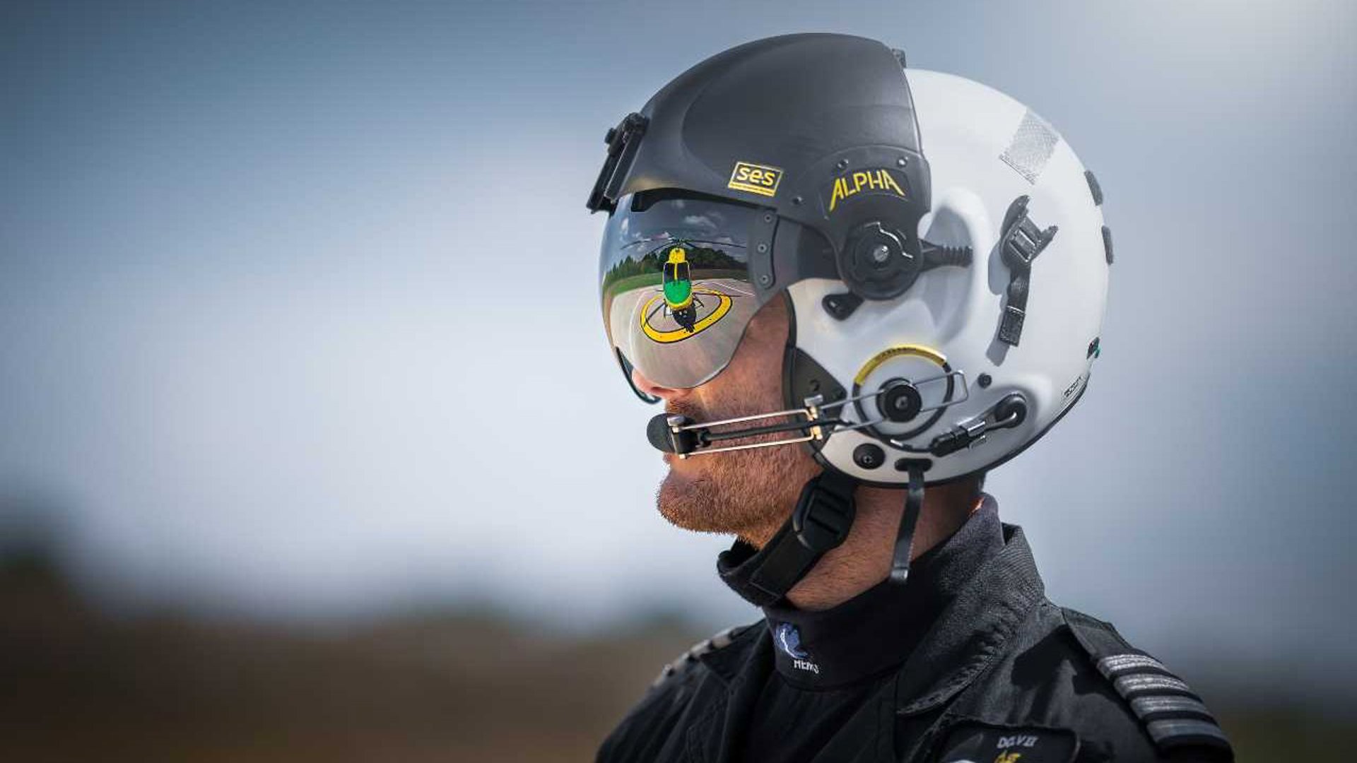 Pilot Rob Collingwood looking at the helicopter whilst wearing a flight helmet and visor. There is a reflection of the helicopter in the visor. Pilot Rob Collingwood looking at the helicopter whilst wearing a flight helmet and visor. There is a reflection of the helicopter in the visor.