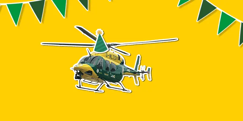 A yellow background with a sticker of the yellow and grey Bell 429 helicopter wearing a cartoon sticker hat, with green bunting around it A yellow background with a sticker of the yellow and grey Bell 429 helicopter wearing a cartoon sticker hat, with green bunting around it