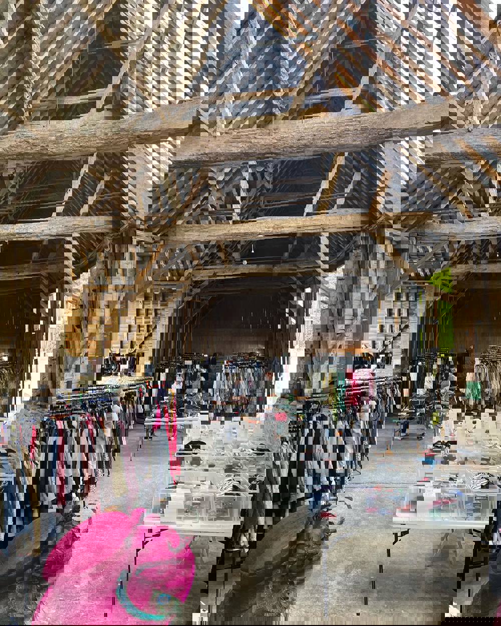 A barn full of clothing rails with boxes of accessories on tables