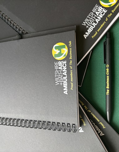 Black notebook and pen with yellow and green Wiltshire and Bath Air Ambulance logo