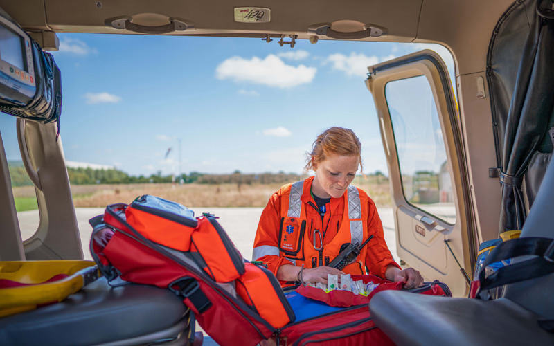 A paramedic looking in a kit bag, which is inside a helicopter