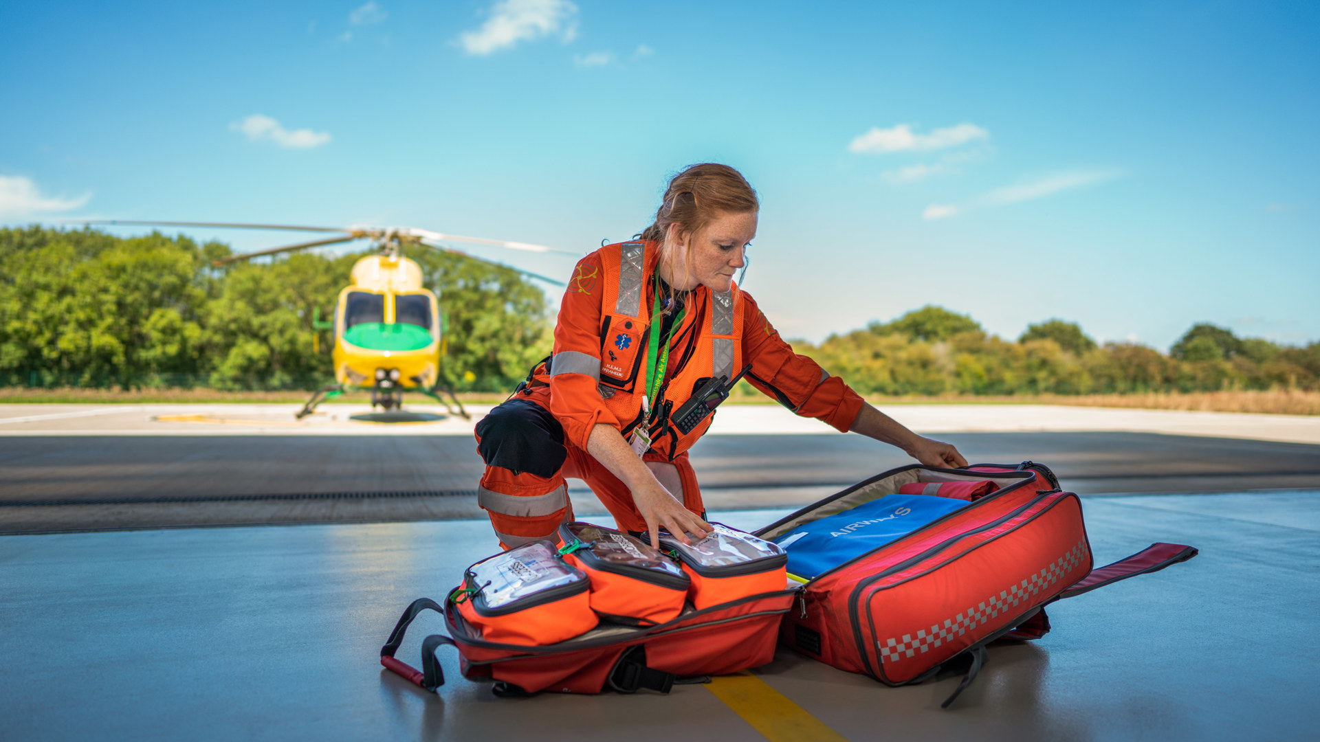 A paramedic on the hangar floor with a kit bag and helicopter in the background