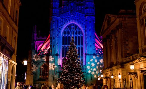 The exterior of Bath Abbey lit up with Christmas lights and a Christmas tree