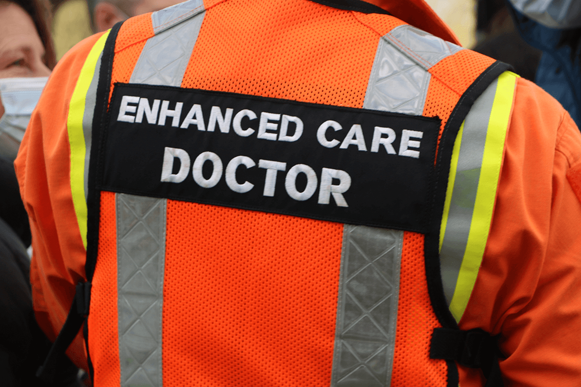 A close up of a person's back wearing and orange flight suit and vest with 'enhanced care doctor' written on the back A close up of a person's back wearing and orange flight suit and vest with 'enhanced care doctor' written on the back