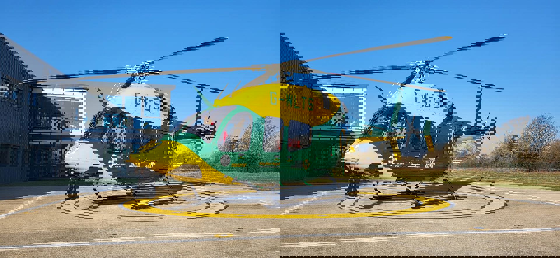 Yellow and green helicopter on helipad with blue sky behind Yellow and green helicopter on helipad with blue sky behind