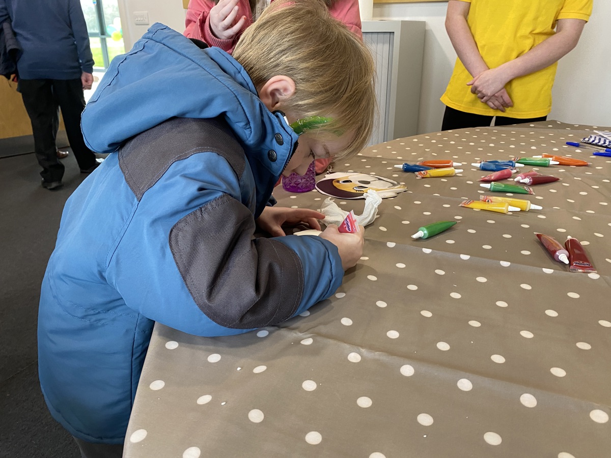 A boy wearing a blue and black jacket, with green glitter face paint, decorating a biscuit A boy wearing a blue and black jacket, with green glitter face paint, decorating a biscuit
