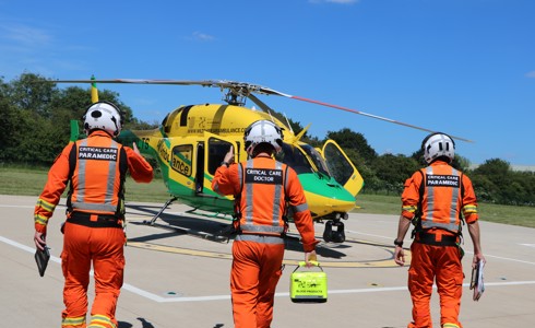 Two critical care paramedics, either side of a critical care doctor, walking towards a yellow and green helicopter