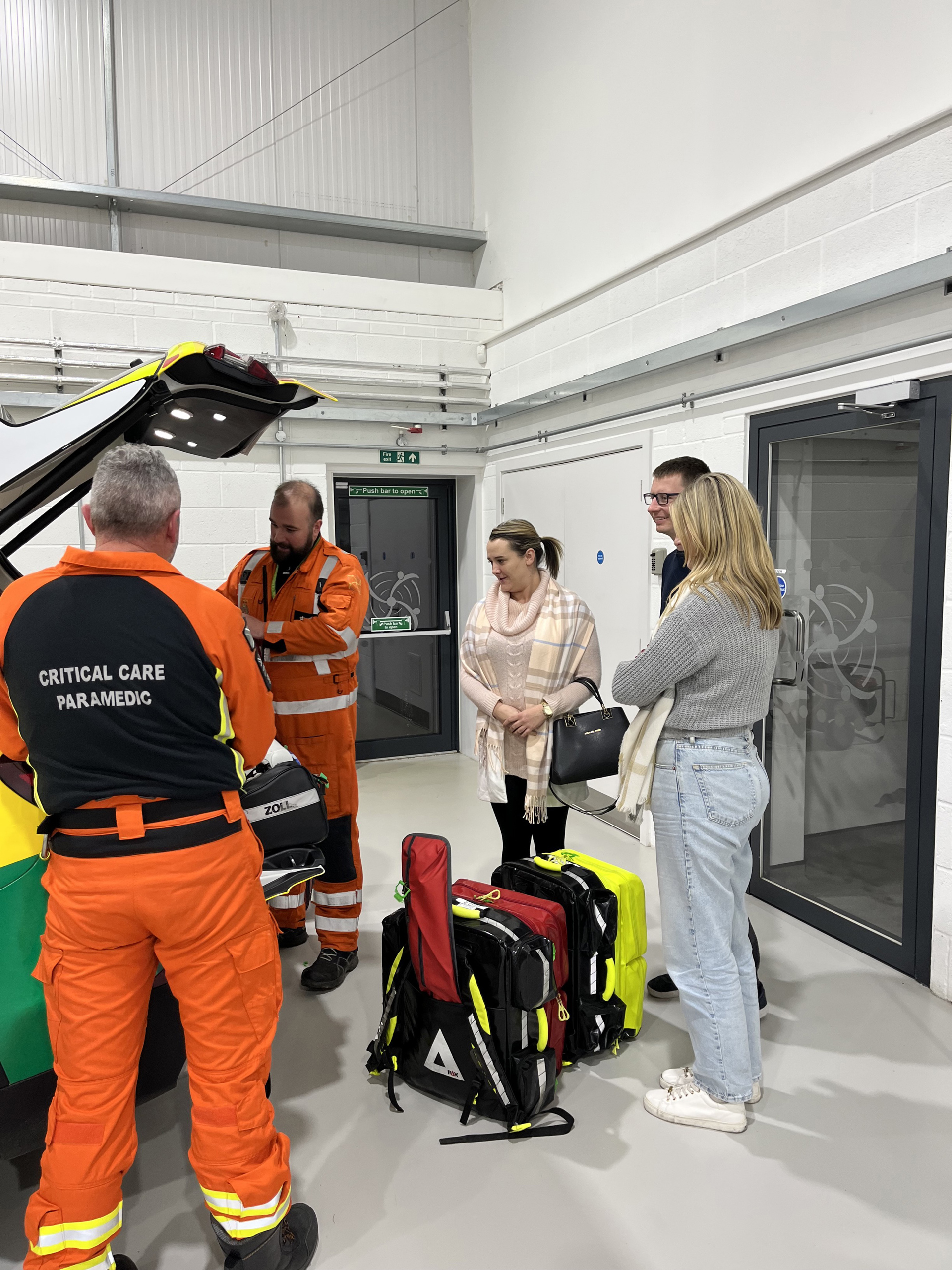 A critical care paramedic wearing orange showing people kit from the back of a critical care car A critical care paramedic wearing orange showing people kit from the back of a critical care car